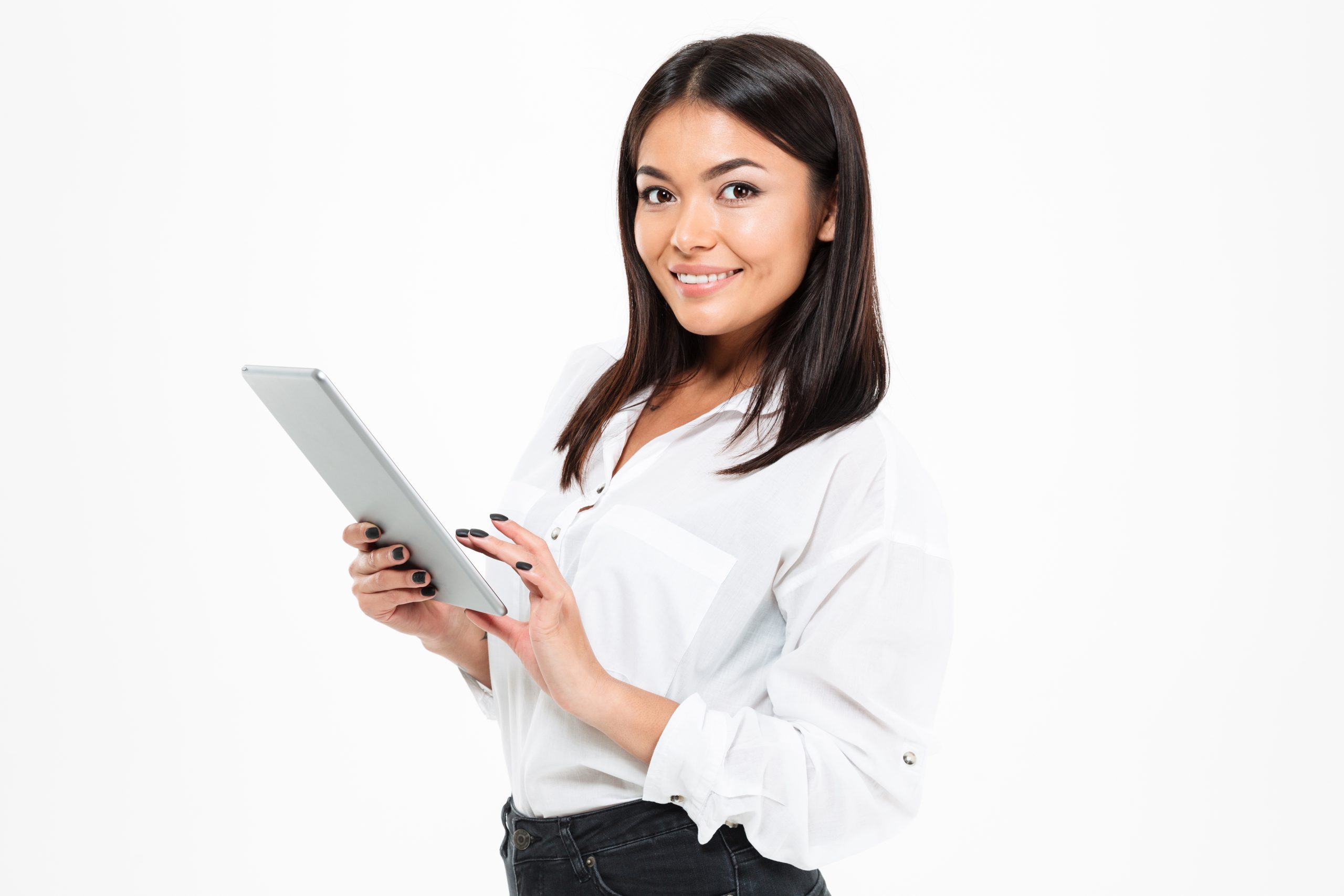 Picture of happy young asian lady standing isolated over white background chatting by tablet computer. Looking camera.